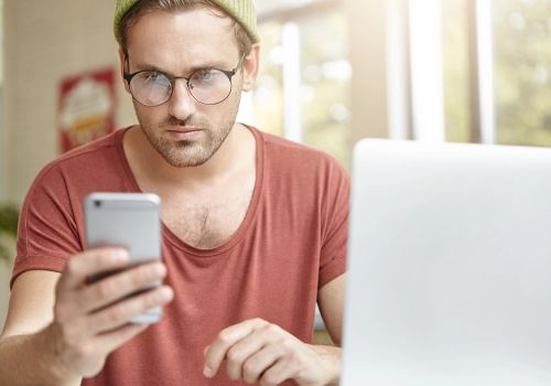 Homem focado mexendo no celular e no computador