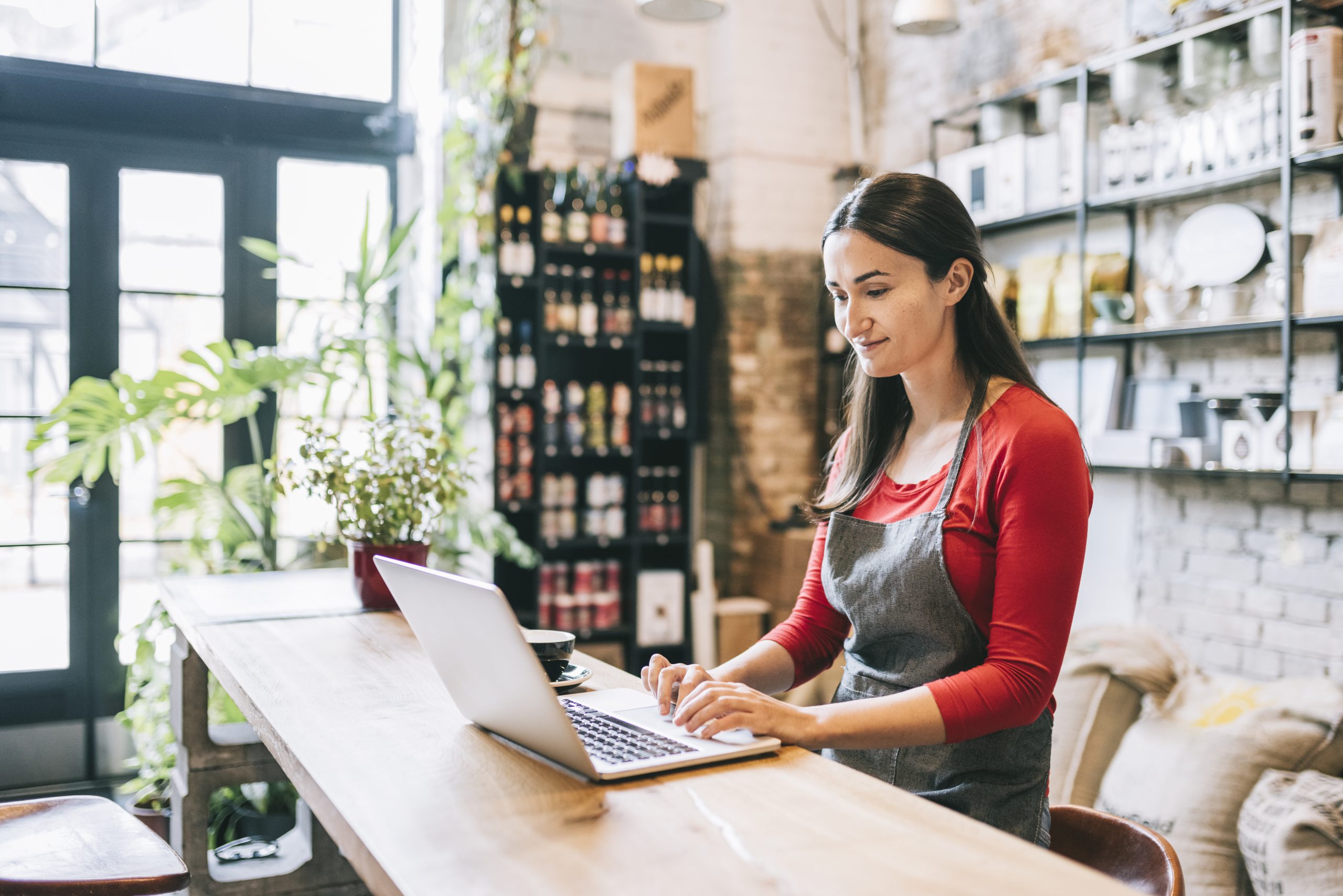 Latin-American woman working on laptop in her small coffee roastery.